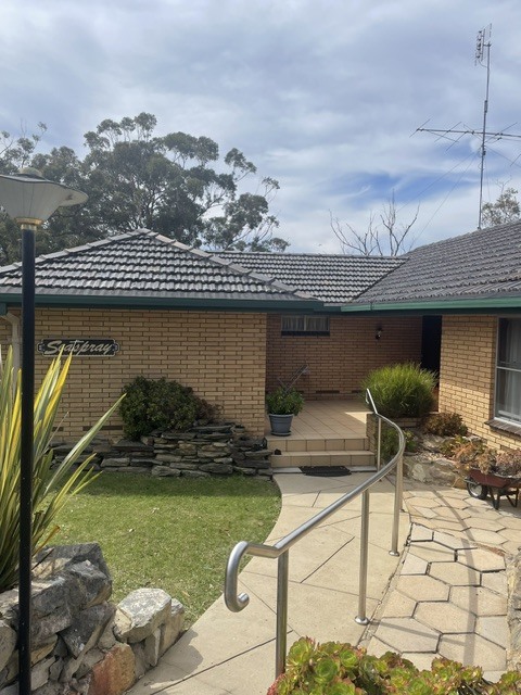 A brick home with a tiled roof, front lawn, sandstone path and handrail