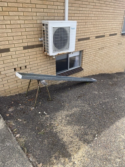 Side of the house with the air-conditioning unit and a length of guttering resting on trestles